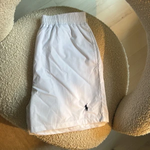 Vita badshorts från Polo Ralph Lauren - Snygga vita badshorts från Polo Ralph Lauren med elastisk midja och innerbyxa i mesh. Fin fräsch färg som passar perfekt till sommaren. Skick-9:10. Storlek:-L men passar mer som M. DMa🤙