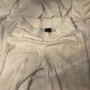 Vita ribbade byxor från Gina Tricot - Säljer ett par vita ribbade byxor från Gina Tricot i storlek XS. Byxorna har en bred resår i midjan och är tillverkade i ett mjukt, stretchigt material. De har raka, vida ben och en snygg ribbad struktur som ger en trendig look.