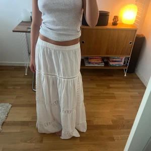 Vit långkjol med spetsdetaljer - Superfin vit långkjol med volanger och spetsdetaljer. Kjolen har resår i midjan och är gjord i ett lätt bomullstyg som känns luftigt. 