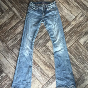 Blå bootcut jeans från Crocker - Snygga blå jeans från Crocker med bootcut passform och låg midja. Klassisk femficksmodell med orange kontrastsömmar och detaljerad knapp. Perfekta för dig som gillar retrostil och bekväma jeans. 