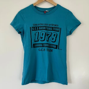T-shirt strl 38 - Bekväm turkos / blå T-shirt i bomull från H&M / Divided med tryck framtill. Trycket visar "Girls College of Sports, G.C.S Basketball Team 1978, Annual Competition, G.C.S Team". Fint skick!!  Hämtas i Stockholm eller skickas mot porto. Kolla gärna mina andra annonser också, kan samfrakta om så önskas. :)