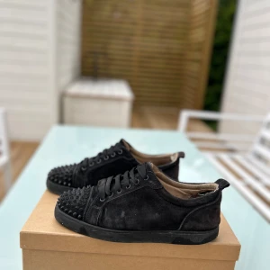 Svarta Louboutin Louis Junior Spikes - Säljer ett par äkta svarta Louis Junior Spikes från Louboutin i mocka med coola nitar på tån. Skorna har snörning och en platt röd sula, vilket ger en edgy vibe. Perfekta för dig som vill sticka ut med exklusiva sneakers i lyxig design.                                                     Har används sparsamt darför fortfarande i ganska bra skick. Det ingår box och även extra nitar och laces. Priset går att diskuteras🙌