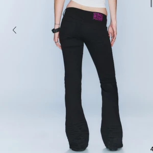 Svarta weekdey bootcut jeans  - Säljer ett par svarta bootcut jeans med snygg lila patch på bakfickan. Jeansen har låg midja och klassisk femficksdesign. Materialet är stretchigt och sitter tajt upptill men släpper ut över benen för en riktigt schysst siluett. Säljer pga köpte för liten storlek.❤️det är storlek 23/32