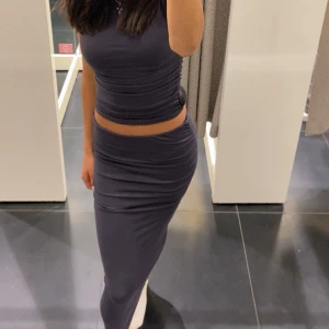 Mörkgrå tight långkjol - Säljer en mörkgrå långkjol med tight passform och ”scrunch” design på sidorna. Kjolen har en enkel, stilren look och är gjord i ett stretchigt material som sitter snyggt mot kroppen. Perfekt för dig som gillar minimalistisk och trendig stil.