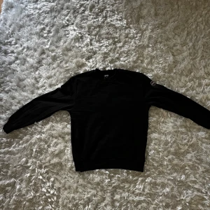 Svart Colmar sweatshirt i bomull - Svart sweatshirt från Colmar med rund hals och diskret logga på ena ärmen. Tröjan är i fint skick och passar bra till alla outfits.