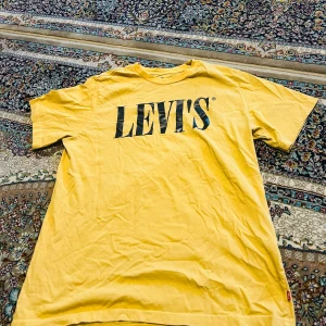 Gul Levi's t-shirt med logga - Gul t-shirt från Levi's i avslappnad passform med stor svart logga framtill. Klassisk rund hals och korta ärmar. Tillverkad i mjuk bomull, perfekt för dig som gillar en enkel men snygg stil. Levi's-röd etikett i sidan för extra detalj.