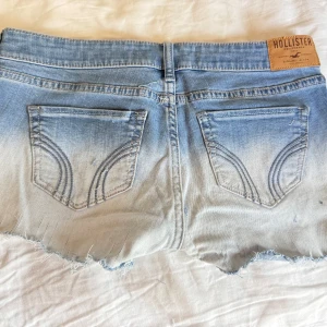 Ljusblå slitna jeansshorts Hollister lowaist - Midjemåttet finns i bild🩵Snygga ljusblå jeansshorts från Hollister med slitna detaljer och fransig kant. Klassisk femficksmodell med låg midja och cool tvätt. Perfekta för varma dagar när du vill ha en avslappnad och trendig look.
