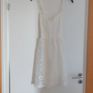 Vit spetsklänning med pärlband - Superfin vit kortklänning med blommig spets och pärlprydda axelband. Klänningen har en feminin v-ringning och markerad midja. Säljer då jag gått ner i vikt och den inte längre passar mig. Fint skick då jag inte använt den mycket, finns en liten fläck dock (se bild tre). pris går att diskutera💞. 
