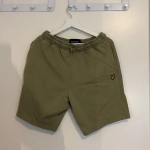 Olivgröna shorts från Lyle & Scott - Snygga olivgröna shorts från Lyle & Scott med elastisk midja och klassisk logga på vänster ben. Mjukt bomullsmaterial, fickor på sidorna och en bakficka. Perfekta för chill dagar eller när du vill ha en avslappnad stil.