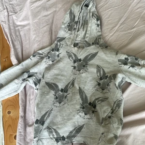 Grå hoodie med kanintryck från Ellos - Supermysig grå hoodie från Ellos med gulligt kaninmönster över hela tröjan. Kaninerna har söta rosetter och trycket är i svart och grått. Tröjan har huva och långa ärmar med muddar. Perfekt för chill dagar eller när du vill sticka ut lite extra. Det ska vara lite svarta prickar överallt det tillhör hoodien den är i storlek 122-128