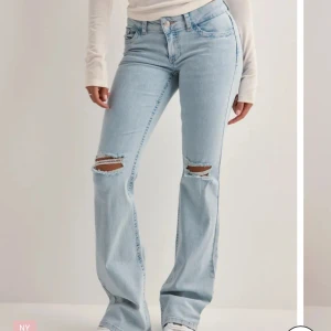 Ljusblå bootcut jeans med slitningar - Snygga ljusblå jeans med bootcut passform och slitna hål vid knäna. Jeansen har klassisk femficksdesign och coola broderade detaljer i rött på bakfickorna. Perfekta för en avslappnad och trendig look.