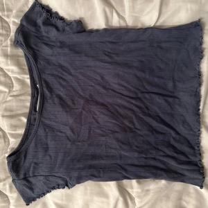 Mörkblå ribbad topp med volangkant - En mörkblå ribbad topp med korta ärmar och volangdetaljer längs ärmslut och nederkant. 