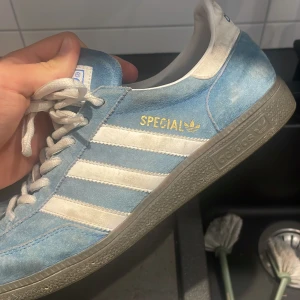 Adidas Spezial blå mockasneakers - Säljer ett par Adidas Spezial sneakers i ljusblå mocka med vita detaljer och klassiska tre ränder på sidan. Skon har snörning, grå sula och guldtexten 'Spezial' på sidan. Perfekt för dig som gillar retrostil och streetwear.