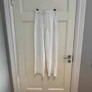 Vita linnebyxor från Gina Tricot - Säljer ett par vita linnebyxor från Gina Tricot med elastisk midja och dragsko. Byxorna har raka, lite loose ben och är perfekta för varma dagar. Lätta och luftiga i materialet, passar dig som gillar en chill och enkel stil.