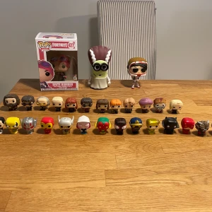 Funko pops - Bilden visar en samling Funko Pop-figurer och små samlarfigurer från populärkultur, inklusive Fortnite, Marvel och andra kända serier. Ingen bok syns på bilden.