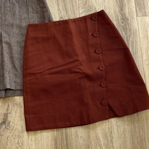 Rostbrun kjol från & Other Stories - Snygg rostbrun kortkjol från & Other Stories med knappar längs sidan och liten slits nedtill. Kjolen är i bomull och har en clean, stilren look som passar perfekt till stickade tröjor eller t-shirts.