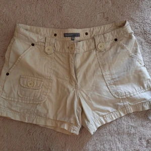 Beige shorts  - Snygga beige shorts från KappAhl med flera stora fickor både fram och bak, dekorerade med knappar. Klassisk passform och midwaist. Perfekta för varma dagar och enkel att matcha med allt. Gjorda i mjuk bomull för en skön känsla.