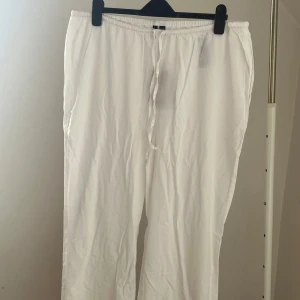 Vita linnebyxor med snören  - Luftiga vita linnebyxor med avslappnad passform och dragsko i midjan. Perfekta för varma dagar när du vill ha något svalt och bekvämt. Byxorna har raka ben och elastisk midja. Storlek 46-48