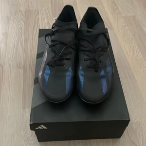 Adidas crazyfast svarta - Säljer ett par svarta adidas fotbollsskor med snygga blå ränder på sidorna. Skorna har snörning och en smidig, låg profil som passar perfekt för snabba rörelser på planen. Tillverkade i syntetmaterial för lätt känsla och bra bollkontroll.