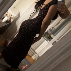 Svart blommig långklänning Bershka - Supersnygg svart långklänning från Bershka med små rosa blommor och korta puffärmar. Klänningen har en figurnära passform, v-ringning och knytband i ryggen. Perfekt för dig som vill ha en feminin och trendig look.