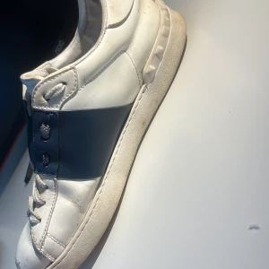 Valentino Open sneakers vit/blå  - Snygga Valentino Open sneakers i vitt skinn med bred blå panel över snörningen. Klassisk rund tå, platt sula och vita skosnören. Perfekta för dig som gillar stilrena och exklusiva sneakers med en sportig touch.