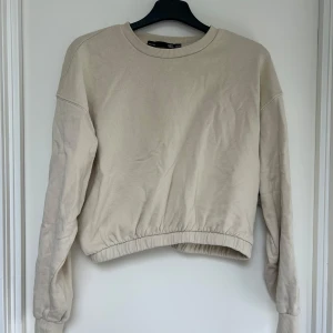 Beige sweatshirt från 157, XS/S - Enkel och stilren beige sweatshirt från 157 i storlek XS/S. Tröjan har rund halsringning, långa ärmar och resår i midjan för en snygg passform. 
