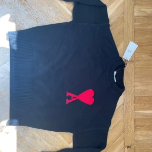 Svart stickad tröja från Ami Paris - Svart stickad tröja  från Ami Paris med röd hjärtlogga på bröstet. Tröjan har storlek S . Har qr kod! Är i väldigt bra kondition!