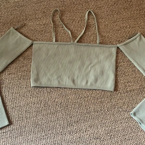 Ljusgrön ribbad offshoulder topp - Säljer en ljusgrön ribbad topp med offshoulder-design, ärmar och smala axelband. Toppen är croppad och har långa avtagbara ärmar. Materialet är mjukt och stretchigt, perfekt för dig som gillar trendiga och bekväma plagg med coola detaljer.