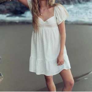 Vit kort klänning  - Supersöt vit kort klänning med broderade små blommor och volang längst ner. Endast använd 1 gång så fin 🥰🥰🥰🥰