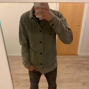 Mörkgrön overshirt från Lindbergh - Säljer en mörkgrön overshirt från Lindbergh med klassisk krage, tre stora fickor framtill och knäppning med svarta knappar. Jackan är i bomull och har en clean, avslappnad look som passar perfekt till jeans eller chinos.