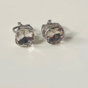 Vintage örhängen med stora stenar - Snygga örhängen med klipsfäste i silverfärgad metall och stora, facetterade glittriga stenar som reflekterar ljuset. Stenarna är fyrkantiga och transparenta med en hint av champagne. Perfekta för att ge din look extra bling och wow-effekt.