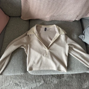 Beige ribbad tröja från H&M - Säljer en beige ribbad tröja från H&M med  krage och v-ringad hals. Tröjan är croppad och har långa ärmar. 