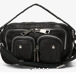 Nunoo väska stor - Cool svart axelväska i skinn med flera silvriga dragkedjor och små fickor framtill. Väskan har en bred, justerbar axelrem och detaljer i metall. Stor och praktisk, då den får plats med mycket saker! 