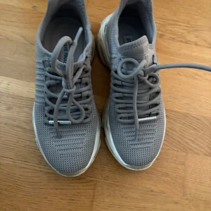 Beiga sneakers från Steve Madden - Snygga beiga sneakers från Steve Madden med stickad ovandel och chunky vit sula. Skorna har snörning och en sportig vibe, perfekta för en trendig streetstyle-look. Ovandelen är i syntetmaterial med stickad känsla för extra komfort.