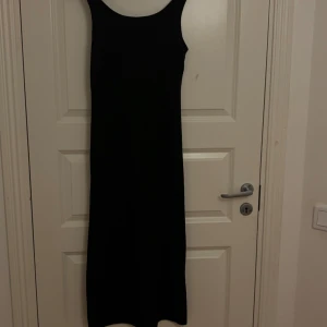 Svart långklänning med breda axelband - Snygg svart långklänning med breda axelband och rundad halsringning. Klänningen har en rak och enkel siluett som ger en stilren look. Perfekt för dig som gillar minimalistisk stil och vill ha en klassisk svart klänning i garderoben.