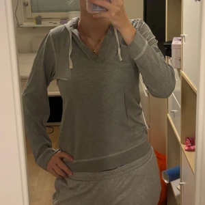 Grå hoodie från H&M med snörning - En enkel och stilren grå hoodie från H&M med vita snören i huvan. Tröjan har lång ärm, normal passform och är tillverkad i mjuk bomullsmix. Perfekt att ha över träningskläder.