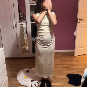 Lång ribbad ljus klänning från H&M - Säljer en snygg långklänning från H&M i ljus beige färg. Klänningen har ribbad struktur, korta ärmar och en tight passform som framhäver figuren. Snygg rynkning vid midjan på sidorna ger extra detalj. Perfekt för dig som gillar stilrena och enkla looks.