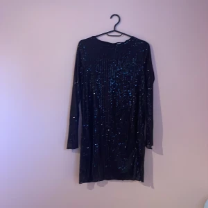 Svart glittrig klänning från Lindex - Snygg svart kortklänning från Lindex med glittriga paljetter över hela klänningen. Modellen har långärmade ärmar och en rak passform. Perfekt för dig som vill sticka ut med lite extra bling! Storlek 158/164, passar dig som är 12-14 år.