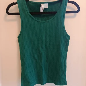 Grön ribbad linnetopp från Divided - Snygg grön ribbad linnetopp från Divided. Modellen är ärmlös med rund halsringning och har en tight passform. Perfekt att styla med jeans eller kjol för en fräsch look.