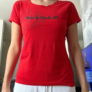 Röd t-shirt med tryck - Snygg röd t-shirt med svart texttryck 'The heart of sport' och diskret sportmönster på bröstet. Modellen är figurnära med rund hals och korta ärmar. Perfekt för dig som gillar sportig stil och vill ha en enkel men cool t-shirt.