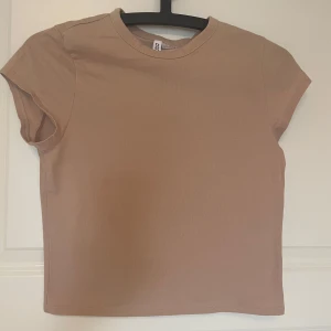 Beige croppad topp  - Snygg beige croppad topp med rund hals och korta ärmar. Enkel och stilren design i mjuk bomull som är skön mot huden. Perfekt att matcha med jeans eller kjol för en chill look. Färgen är neutral och passar till allt.