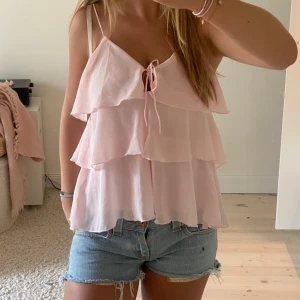 Helt ny ljusrosa volangtopp  - Supersöt ljusrosa volangtopp från Sinsay med tunna axelband, flera lager volanger och knytning framtill. Storlek xs, passar även s😊