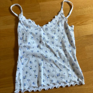 Blommig ribbad linnetopp Hollister S - Supersöt vit ribbad linnetopp från Hollister med små blå blommor och detaljer