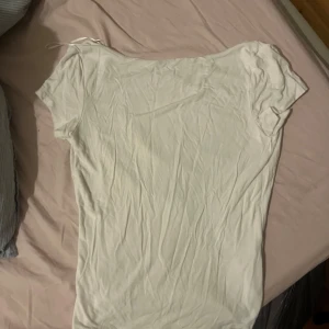 Vit topp med djup rygg från Gina Tricot - En vit, enkel topp från Gina Tricot med korta ärmar och en riktigt djup, öppen rygg. Tunt och mjukt material som känns skönt mot huden. Perfekt för dig som gillar minimalistisk stil men ändå vill ha en cool detalj med den öppna ryggen.