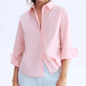 Ljusrosa skjorta i bomull - Snygg ljusrosa skjorta med klassisk krage och knappar framtill. Skjortan har en avslappnad passform och trekvartsärmar som kan vikas upp för en chill look. Perfekt att styla med jeans eller kjol för en fräsch vibe.