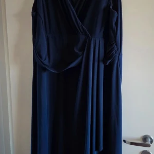 Marinblå klänning Fashion New-York - Använd vid ett tillfälle. Snygg marinblå klänning från Fashion New-York med omlott överdel och korta ärmar. Klänningen har draperad detalj i midjan och är tillverkad i ett mjukt stretchigt material av polyester och elastan. Perfekt för dig som vill ha en elegant och bekväm look.