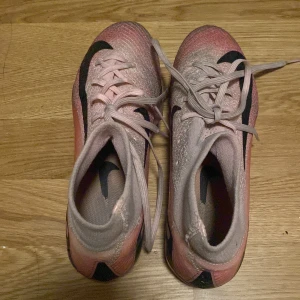 Nike rosa fotbollsskor med snörning - Säljer ett par snygga Nike fotbollsskor i rosa med svarta detaljer och snörning. Skorna har en smidig, strumpliknande passform och mönstrad sula för bra grepp på planen. Perfekta för dig som vill sticka ut på matchen! Säljs för att de är förr små på mig nu. Priset kan sänkas.