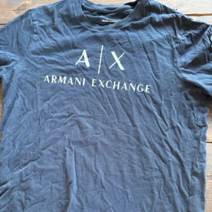 Svart t-shirt från Armani Exchange - Snygg svart t-shirt från Armani Exchange med vit logga framtill. Modellen är slim fit och har klassisk rund hals och korta ärmar. Tillverkad i mjuk bomull som känns skön mot huden. Perfekt för dig som gillar stilrena och trendiga plagg.
