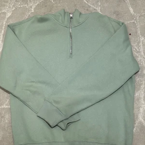 Grön half zip sweatshirt från H&M - Snygg ljusgrön sweatshirt från H&M med relaxed fit. Tröjan har half zip-dragkedja vid halsen och långa ärmar med breda muddar. Perfekt för en chill och avslappnad stil. Tillverkad i mjuk bomullsmix som känns skön mot huden.