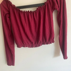 Ribbad offshoulder topp från Bik Bok - Två snygga ribbade offshoulder-toppar från Bik Bok i storlek S. Ena är vinröd och andra är mörkgrön, båda med långa ärmar och volangkant vid halsringning och nederkant. . 20 kr styck